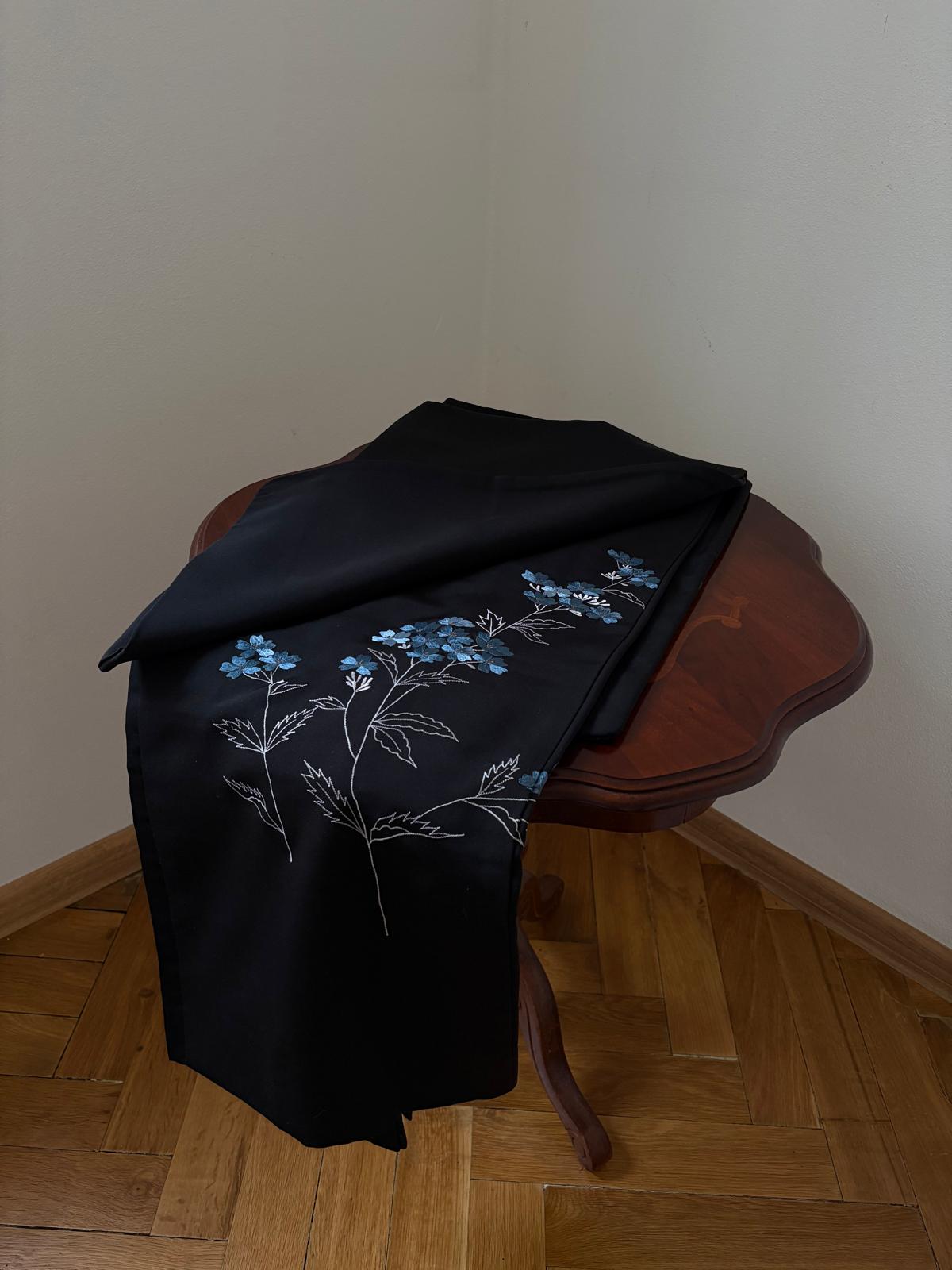 Black kimono with blue floral embroidery arranged on a wooden table